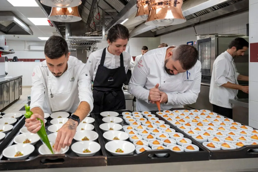 Three chefs filling dozens of lined-up bowls with a piping bag