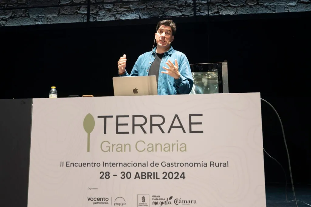 Speaker gesturing behind the Terrae Gran Canaria sign on stage