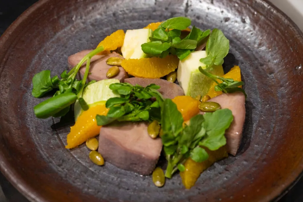 A dish of meat with orange and shoots served in a rustic bowl