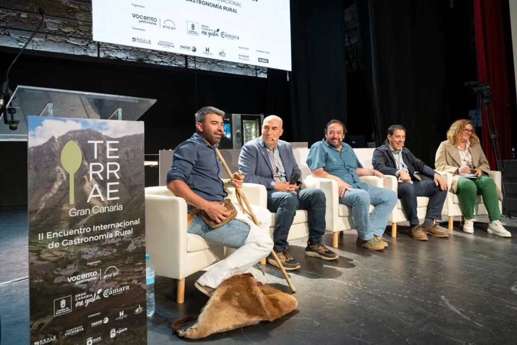 Round table with five participants, a shepherd’s crook and a sheepskin on stage