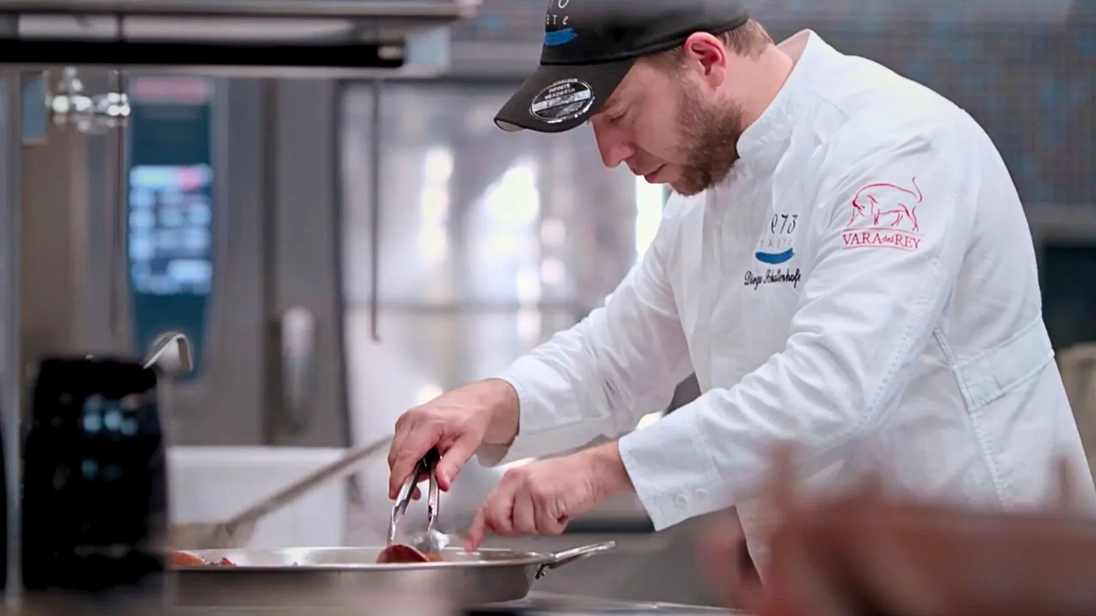 Diego Schattenhofer cooking in his Taste 1973 chef's jacket, wearing the Vara del Rey emblem