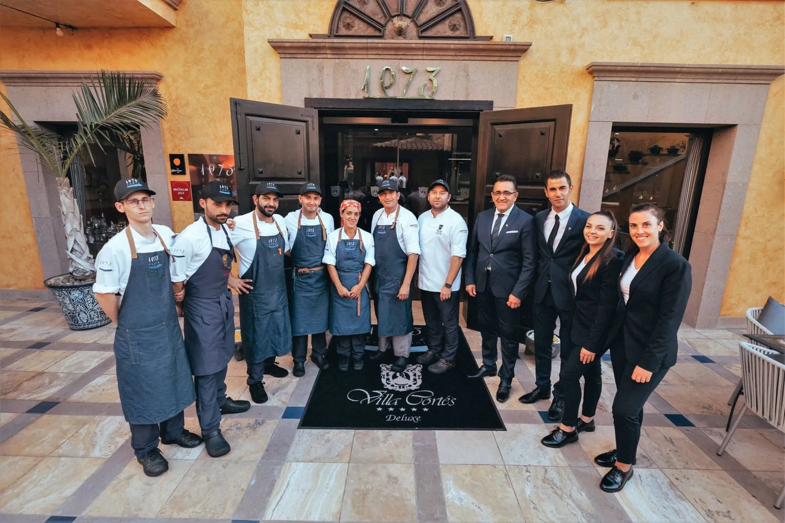 The front-of-house and kitchen team of Taste 1973 posing at the restaurant entrance, under the '1973' sign