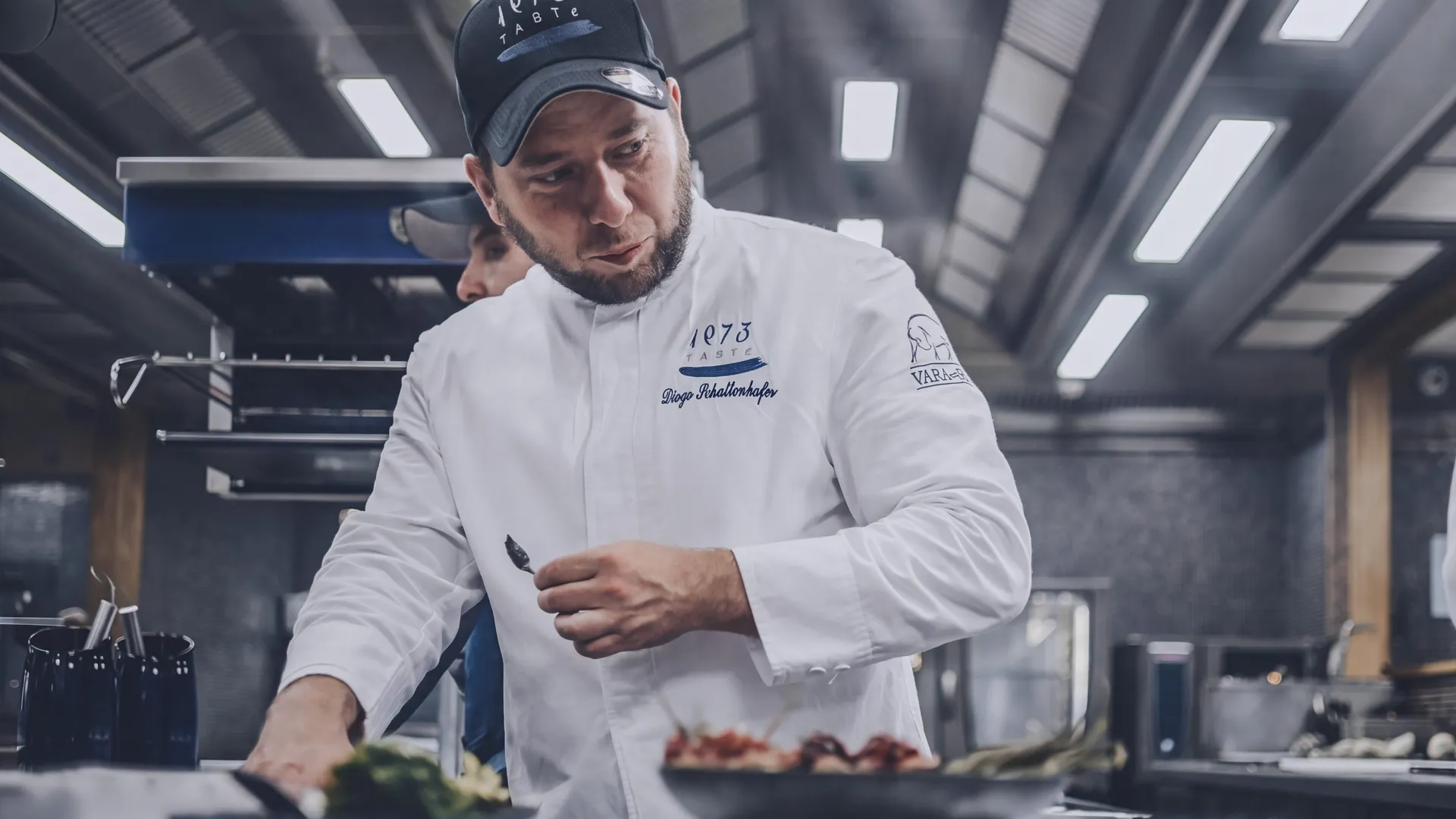 Diego Schattenhofer, in a Taste 1973 cap, finishing a dish at the kitchen pass of the restaurant