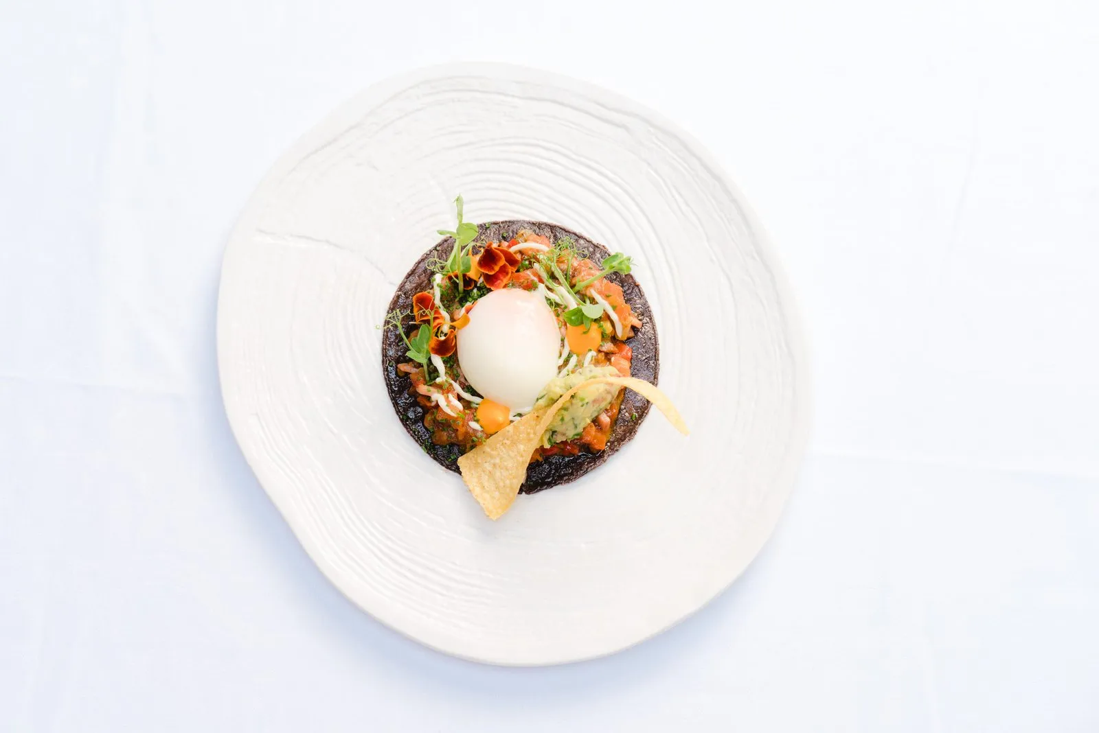 White ceramic plate with a dark base, poached egg, shoots and flowers, seen from above