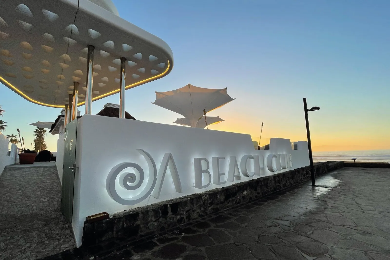 The OA Beach Club sign on the terrace's white wall, at sunset by the sea