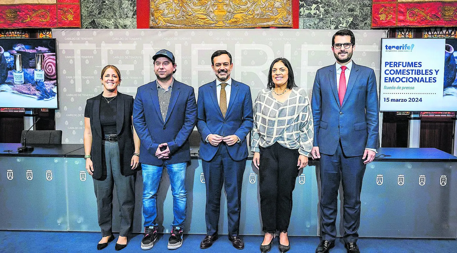 Press conference presenting the edible and emotional perfumes, with five people in front of a Cabildo de Tenerife panel