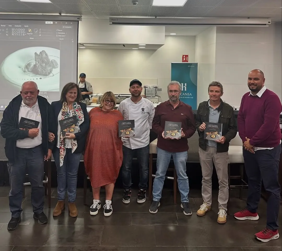 Six people pose holding a copy of the book during its launch, in front of a screen showing a projected dish
