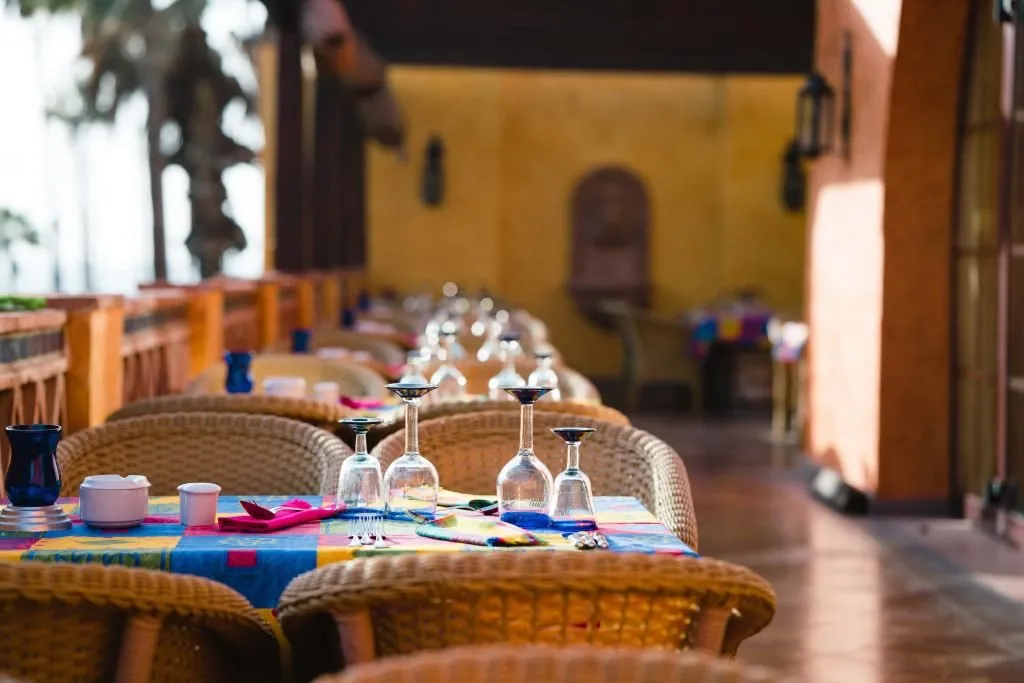 Tables at the Pancho Villa restaurant with colourful tablecloths, glassware and wicker chairs, on a terrace with yellow walls