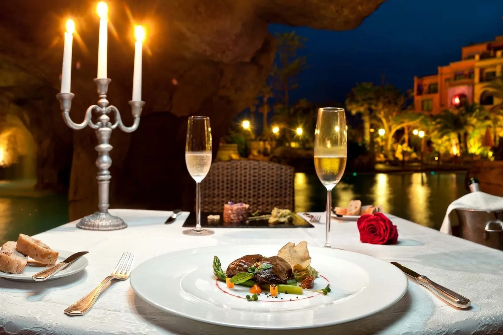 A table at the Tiziano restaurant set for dinner, with a candelabra, glasses and views over the hotel's illuminated gardens