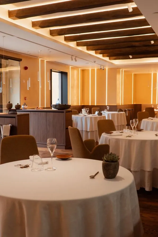 The Taste 1973 dining room: round tables dressed in white beneath wooden beams and warm light