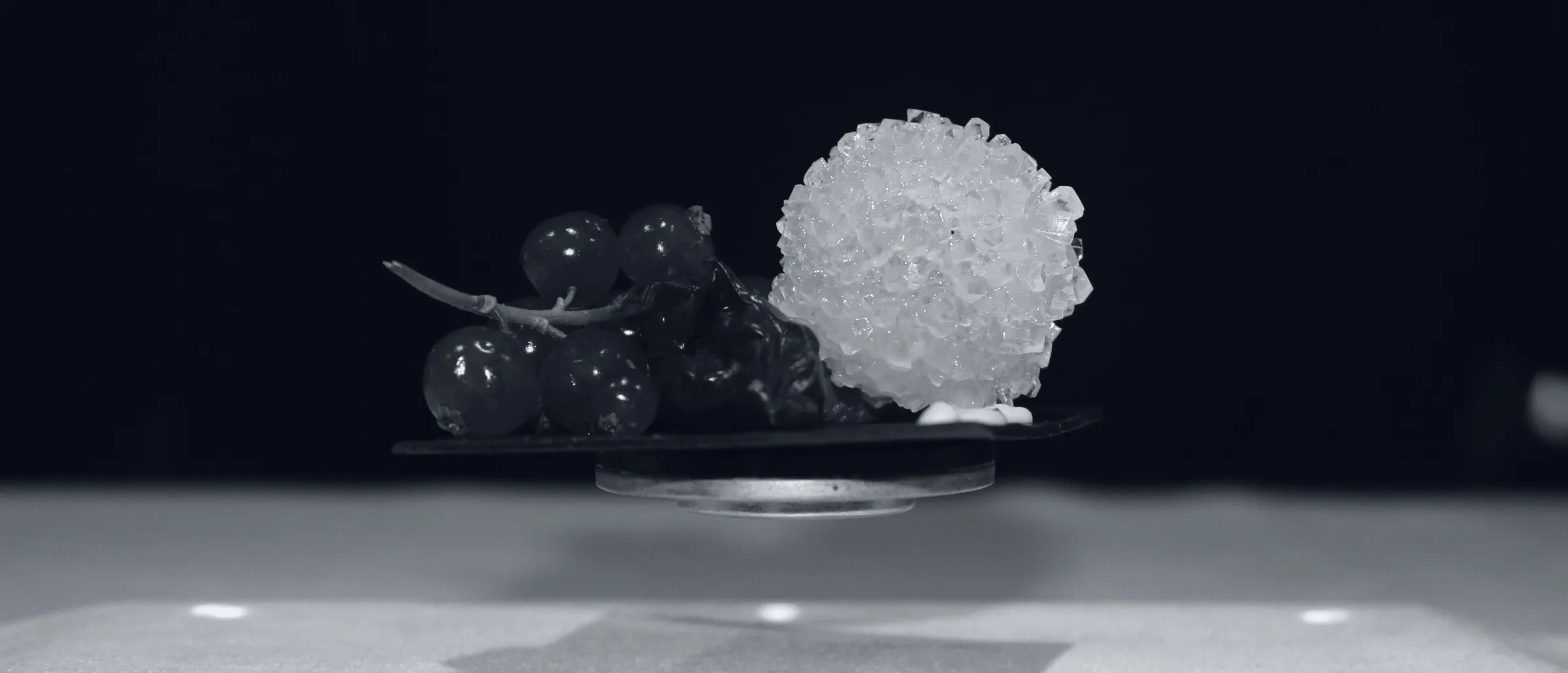 A redcurrant tapa and a crystallised sphere suspended in the air above a table, with no visible support
