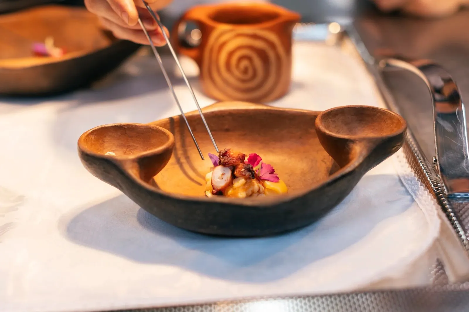 A cook finishes a bite with tweezers over a clay gánigo (a traditional Canarian earthenware bowl) at the Taste 1973 pass