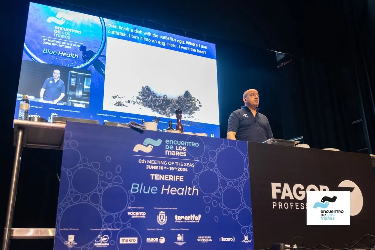 Talk on the stage of the VI Encuentro de los Mares, with the screen projecting a cooking preparation